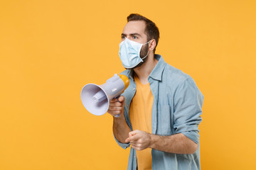 Young man in sterile face mask posing isolated on yellow background in studio. Epidemic pandemic...