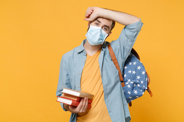 Tired young man in sterile face mask with backpack posing isolated on yellow background in studio....