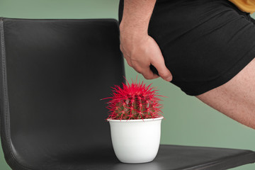 Young man and chair with cactus on color background, closeup. Hemorrhoids concept