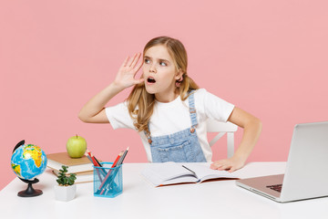 Obraz na płótnie Canvas Shocked little kid schoolgirl 12-13 years old study at desk with pc laptop isolated on pink background. School distance education at home during quarantine concept. Try to hear you with hand near ear.