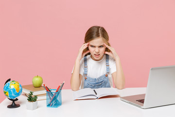 Displeased tired little kid schoolgirl 12-13 years old study at white desk with pc laptop isolated on pink background. School distance education at home during quarantine concept. Put hands on head.