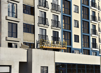 Obraz premium Suspended construction cradle on the background facade of the building. Mobile scaffolding platform for construction work at height, facade cleaning, plastering. Insulation and wall painting, cladding
