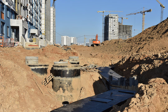 Laying Concrete Manholes And Heating Drain Pipes And For Stormwater System In Trench At Construction Site. Sewerage Manhole And Pipes Line Under Construction.  Chambers And Pump Station