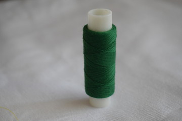 A spool of green thread. Sewing items.