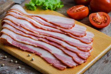 Raw sliced bacon on wooden board.