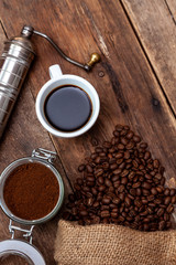 Bag of coffee on a wooden table. Coffee beans ground in a jar. Manual coffee grinder. Top view, place for text. Brown background. Packing coffee in a pack. White up with a drink.