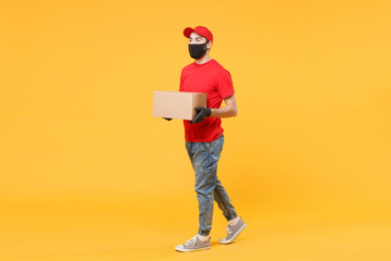 Delivery man employee in red cap blank t-shirt uniform face mask glove hold empty cardboard box...