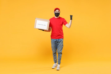 Delivery man employee in red cap blank t-shirt uniform face mask glove hold donations cardboard box isolated on yellow background studio Service quarantine pandemic coronavirus virus 2019-ncov concept