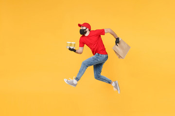 Fun jumping delivery man guy employee in red cap mask gloves hold craft paper packet food coffee...