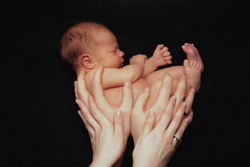 Newborn baby lying on parents hands. Naked newborn baby
on the black background. Love and warmth of...