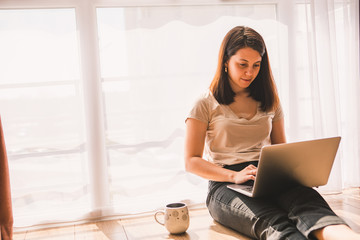 Obraz premium woman sitting on the floor working on laptop near big window