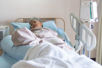 Obraz premium Healthcare and medical patient concept, Elder Asian people sick sitting alone on bed in hospital with medical drip intravenous needle, give salt water when her get well after treatment or surgery
