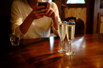 レストランの席でスマホを触る男性とテーブルの上にシャンパングラス２つ