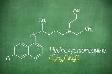 Hydroxychloroquine , chloroquine medicine substance. Drug introduced as treatment for coronavirus SARS-CoV-2. Active in COVID-19 supportive therapy. Chemical formula written with chalk on board.