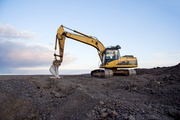 Excavator working at open pit mining on sunset background. Backhoe digs gravel in sand quarry on...