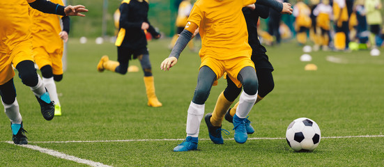 Fototapeta na wymiar Group of Young Boys in Soccer Sportswear Running and Kicking Ball on the Soccer Grass Field. Low Angle Image of Youth Football Competition with Blurred Stadium Background