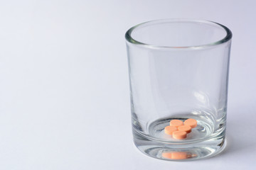 Orange color tablet pills in glass on white background.