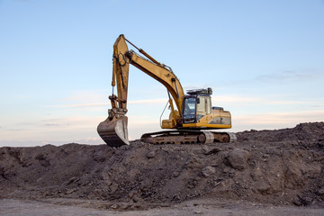 Excavator working at open pit mining on sunset background. Backhoe digs gravel in sand quarry on...