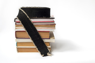 A black belt in martial arts on a stack of books on the study of martial arts of aikido, karate,...