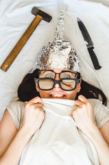 Paranoid young woman wears foil hat and sleeps with weapon and different glasses because of mental...