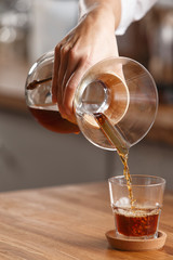 pour coffee into a glass on a wooden table