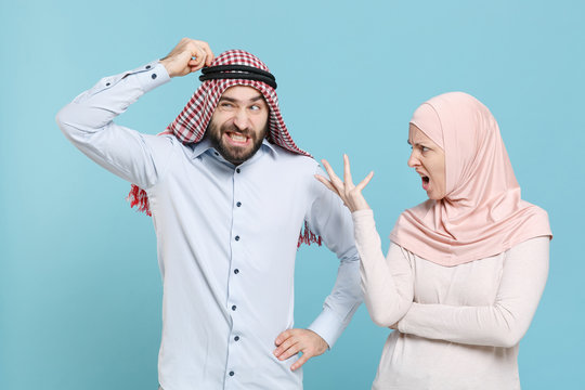Preoccupied displeased couple friends arabian muslim man wonam in keffiyeh kafiya ring igal agal hijab clothes isolated on blue background. People religious concept. Spreading hands, put hand on head.