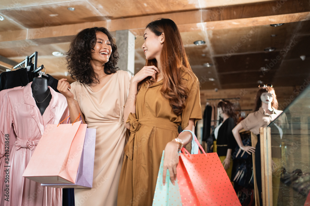 Wall mural happy woman in the fashion shopping centre holding paper bag with friend while walking