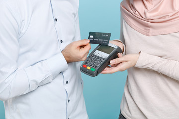 Obraz na płótnie Canvas Cropped image of young arabian muslim man wonam in casual clothes isolated on blue background. People religious concept. Hold modern bank payment terminal to process and acquire credit card payments.