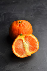 Ripe juicy tangerines on black background. Half of a fruit and one whole.