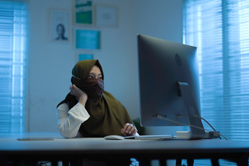 beautiful Muslim Asian wearing green headscarves and mask, work from home in modern interior design...