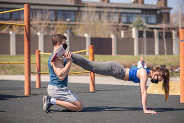 Athletic guy doing bench press with his girlfriend. Do exercises in medical masks during a pandemic. COVID-19. Health care.