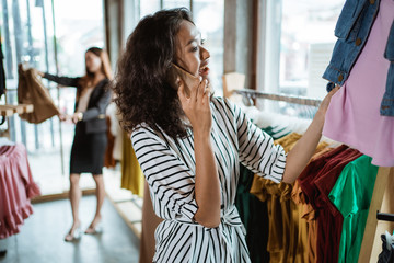 beautiful young asian fashion shop owner at her boutique checking some product while making a phone call