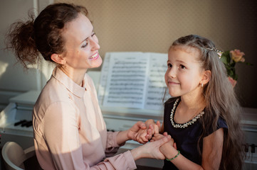 Home piano lesson. A woman and two girls practice sheet music on one musical instrument. Family concept. The idea of activities for children during quarantine.