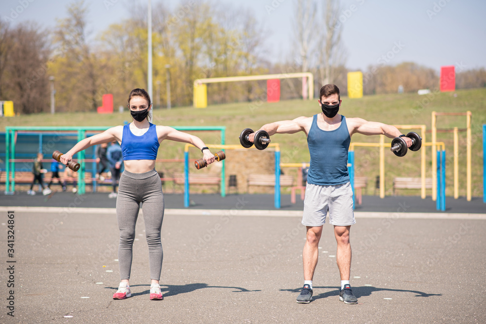 Wall mural athletic guy and girl doing exercises with dumbbells on the sports field in medical masks. covid-19.