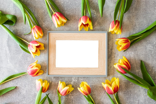 Empty picture frame next to flowers on grey background.