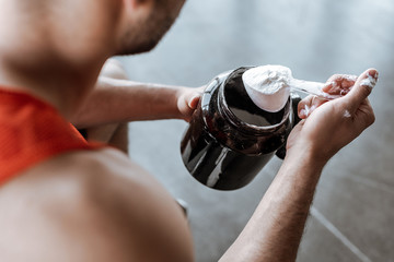 cropped view of sportsman holding jar and measuring spoon with protein powder
