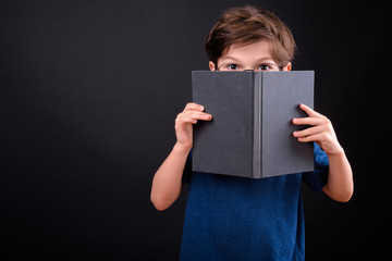 Portrait of shy young boy covering face with book