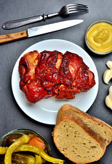 Roasted smoked pork knuckle with mustard, garlic, pickles and goat horns pepper vegetable on slate slab. Top view.