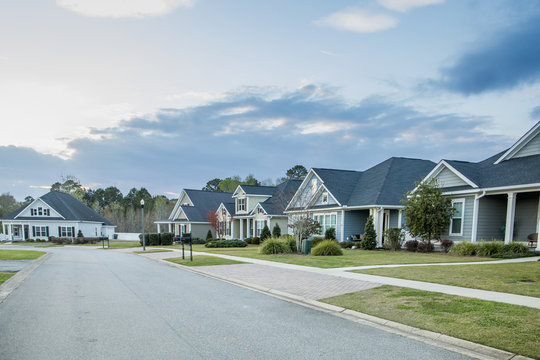 A street view of a new construction neighborhood with larger landscaped homes and houses with yards and sidewalks taken near sunset with large clouds in the sky