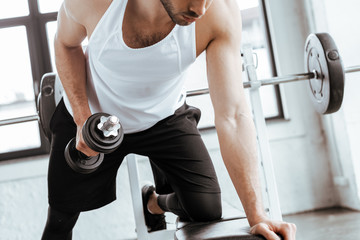 cropped view of bearded man exercising with heavy dumbbell in gym