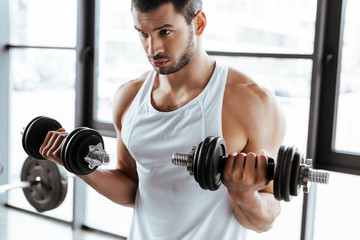 bearded sportsman exercising with dumbbells in gym