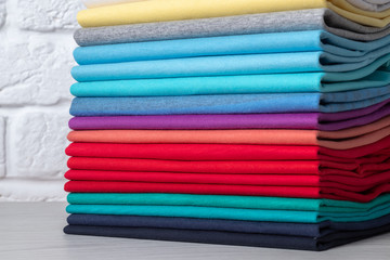 A stack of clean, neatly folded colored clothes on a light wooden table. Colors of rainbow.