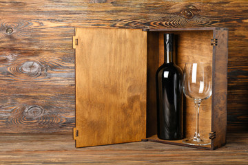 Box with bottle of wine and glass on wooden background