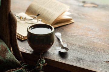 Cup of coffee, old book and glasses on the windowsill, near a chair with a plaid