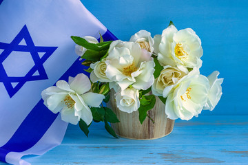 Flag of Israel and white roses on blue wooden background. Independence Day celebration.