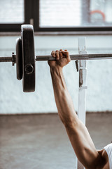 Naklejka premium cropped view of sportsman working out with barbell in gym