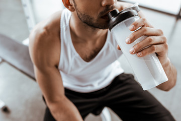 Obraz premium przycięty widok sportowca pije koktajl białkowy trzymając butelkę sportową