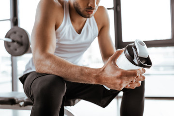 Fototapeta na wymiar cropped view of sportsman holding sports bottle with protein milkshake in gym