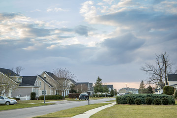 Obraz premium A street view of a new construction neighborhood with larger landscaped homes and houses with yards and sidewalks taken near sunset with copy space