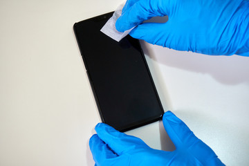 Close-up of a human hand in blue gloves cleaning smartphone screen with an alcohol wipe, prevent infection of COVID-19 coronavirus